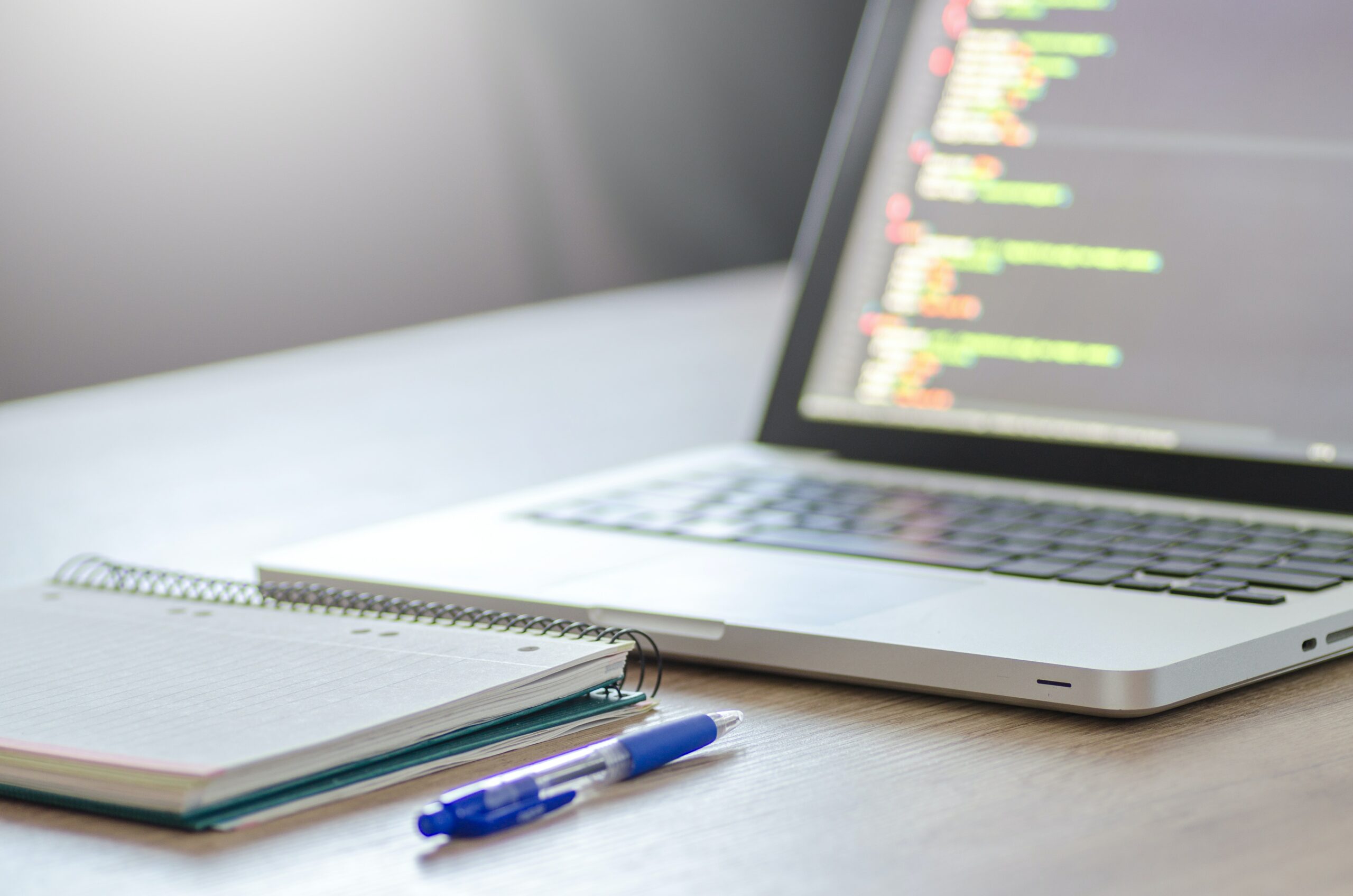 An image of a laptop, notebook and pen